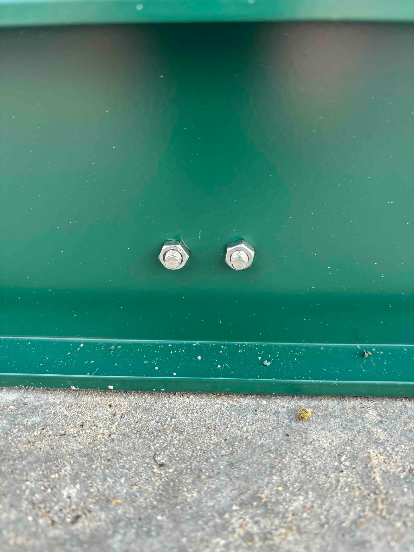 Two anchor bolts securing a green greenhouse aluminum frame to concrete base