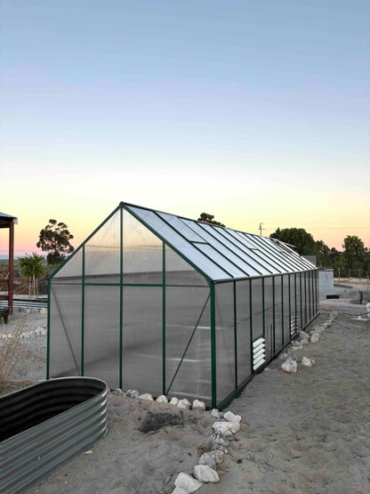 Large aluminium-frame greenhouse with polycarbonate panels in a sandy outdoor setting at sunset