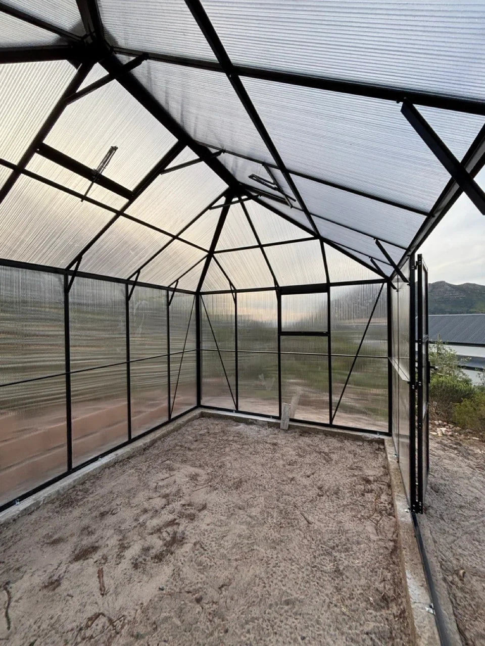 Greenhouse with transparent roof and walls, surrounded by a natural landscape.