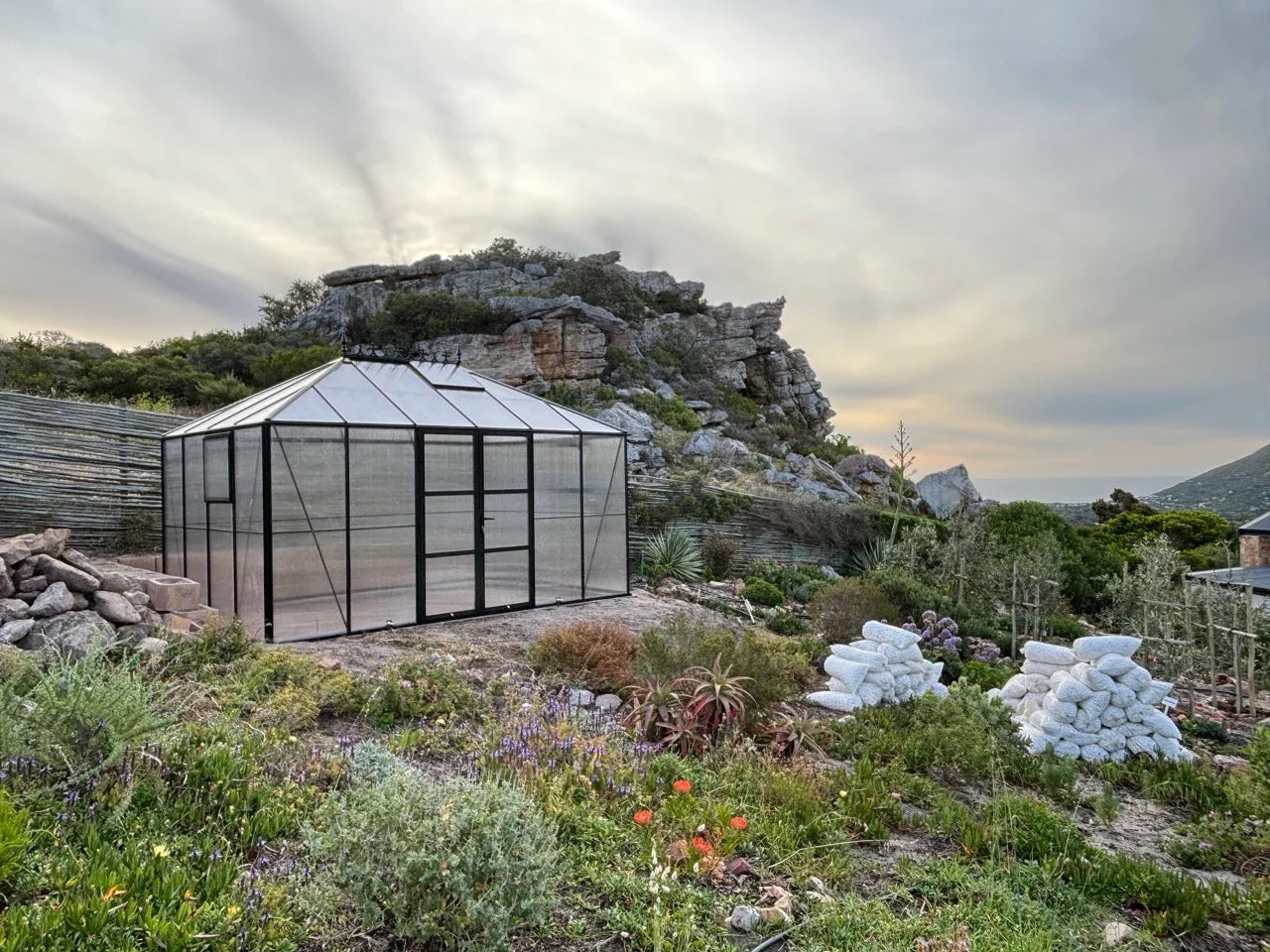 Greenhouse in a natural setting with mountains and sky.