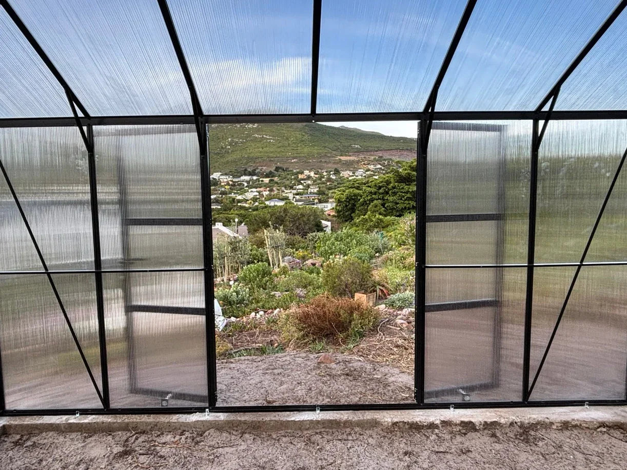 Greenhouse with transparent roof and walls overlooking a scenic landscape.