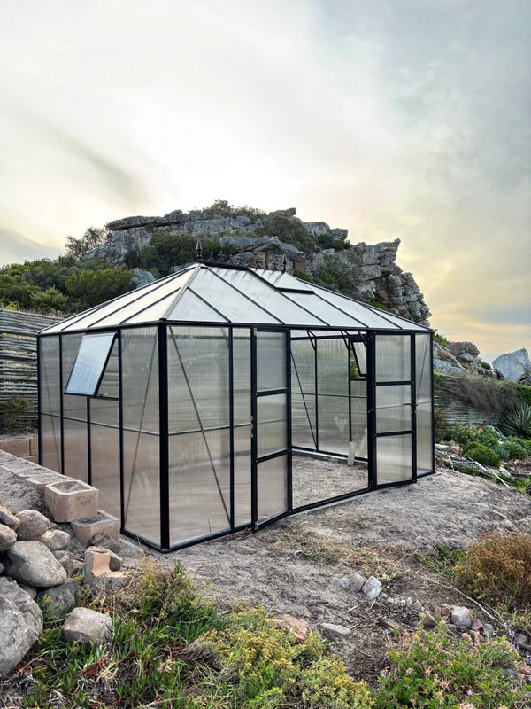 Hexagonal greenhouse in a natural setting with rocks and plants.