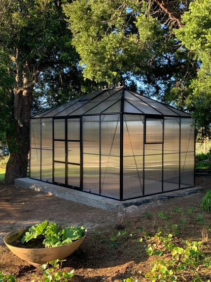 Large Black Polycarbonate greenhouse in a garden setting with trees and plants around