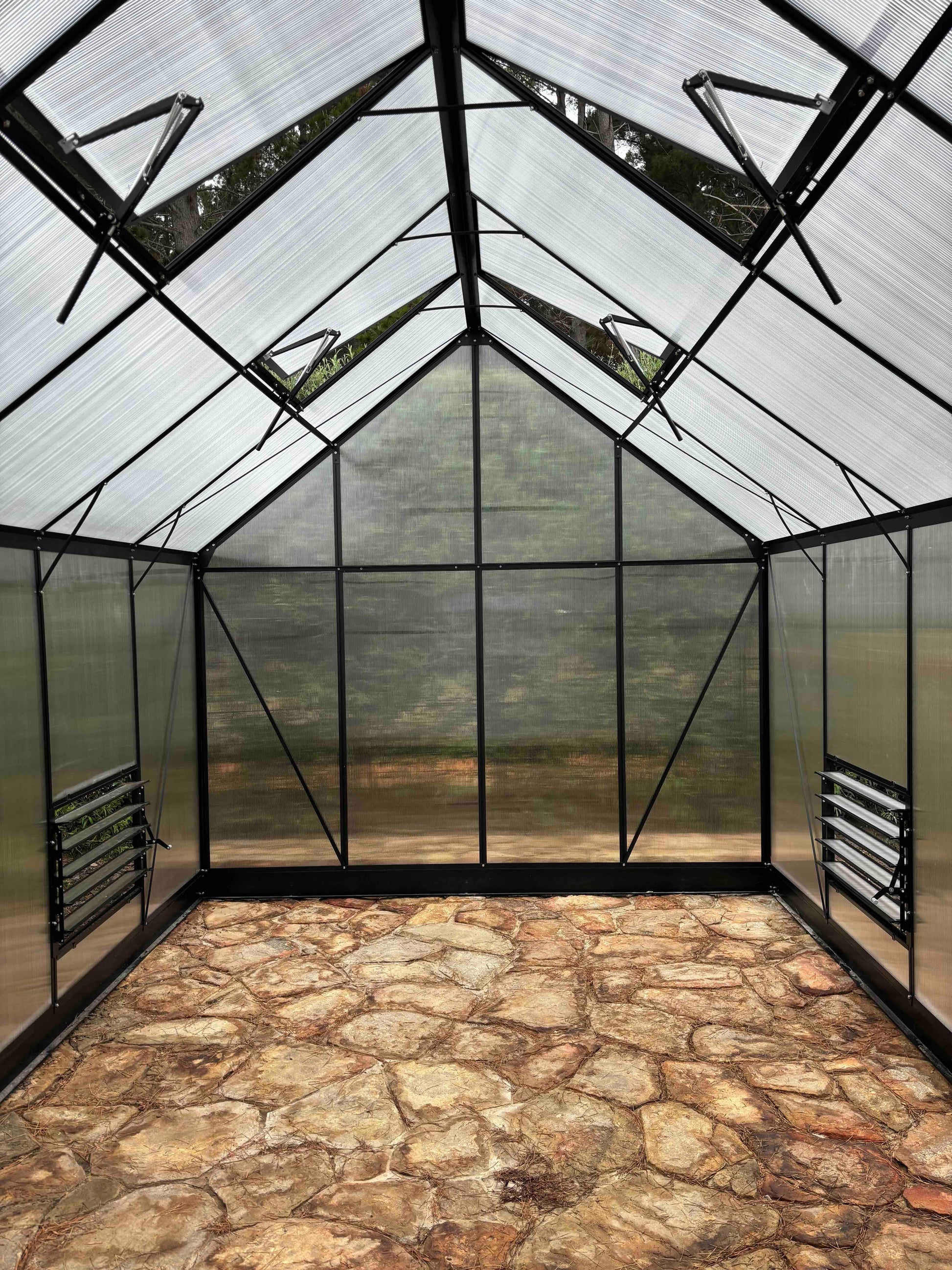 Inside view of a polycarbonate-panel greenhouse with stone floor and aluminium frame