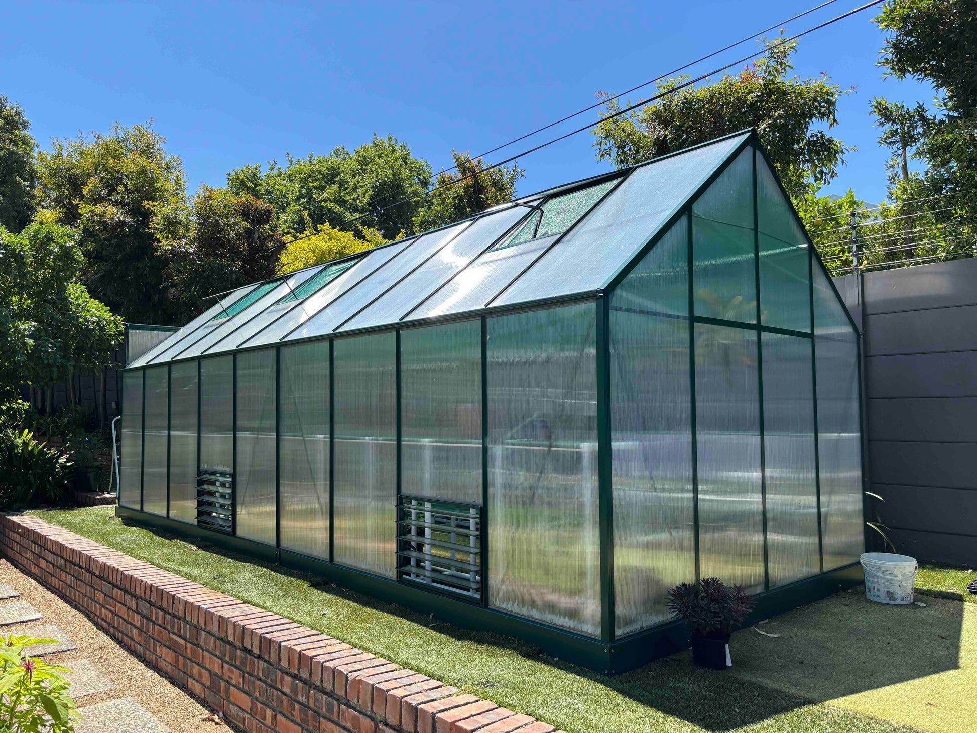 Aluminium frame greenhouse with clear polycarbonate panels in a sunny garden setting