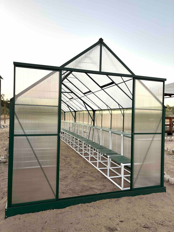 Greenhouse with transparent walls and a green frame on a sandy ground.